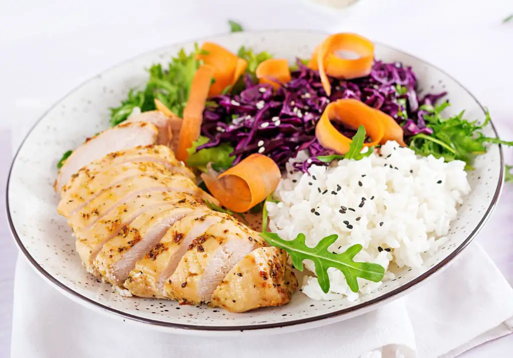 Buddha bowl dish with chicken fillet, avocado, red cabbage, carrot, fresh lettuce salad and sesame.