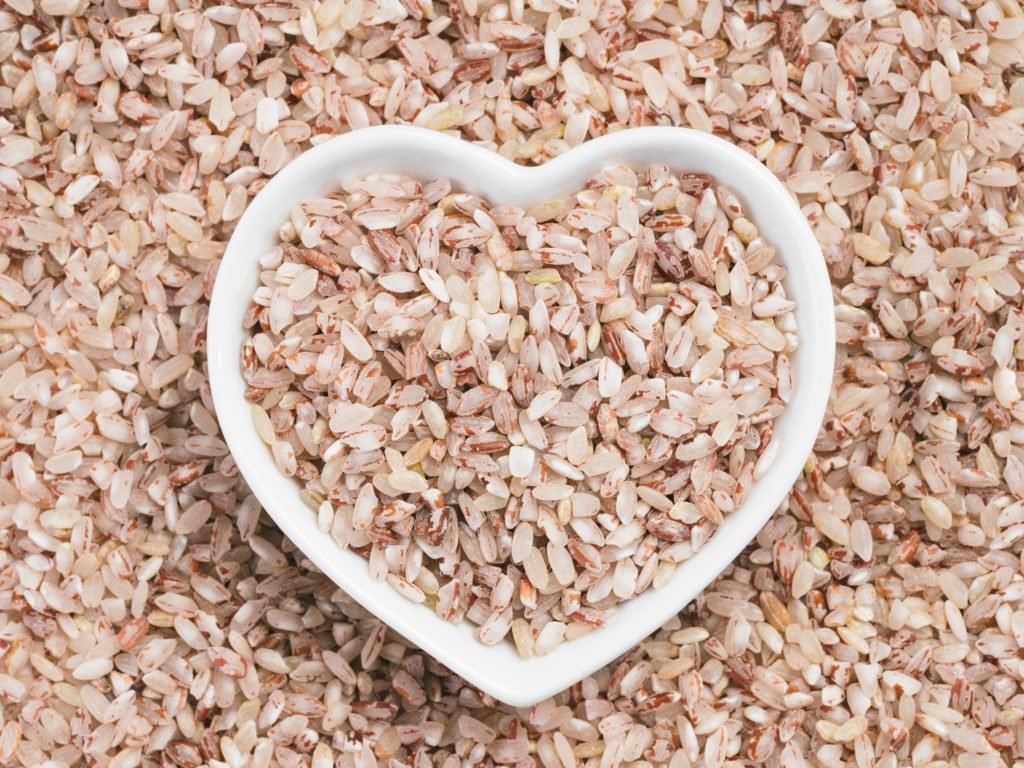 Red rice in heart-shaped bowl on rice background