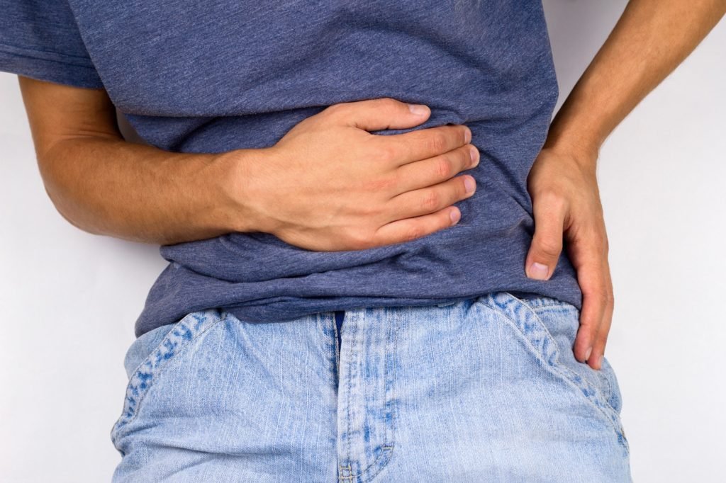 young man in jeans and t-shirt holds hands to his stomach and back