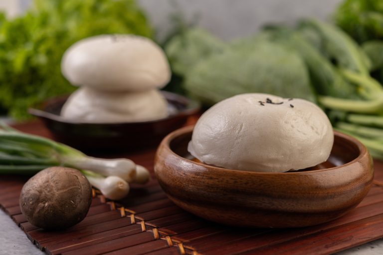 Steamed buns in a wooden dish on a wooden grill.