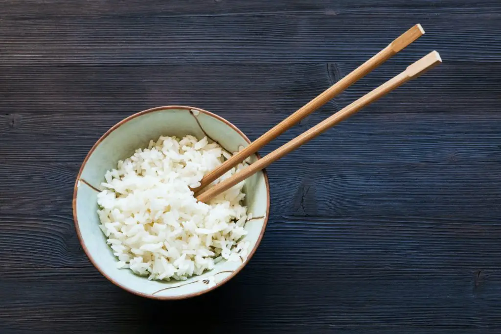 chopsticks in bowl with boiled rice on dark