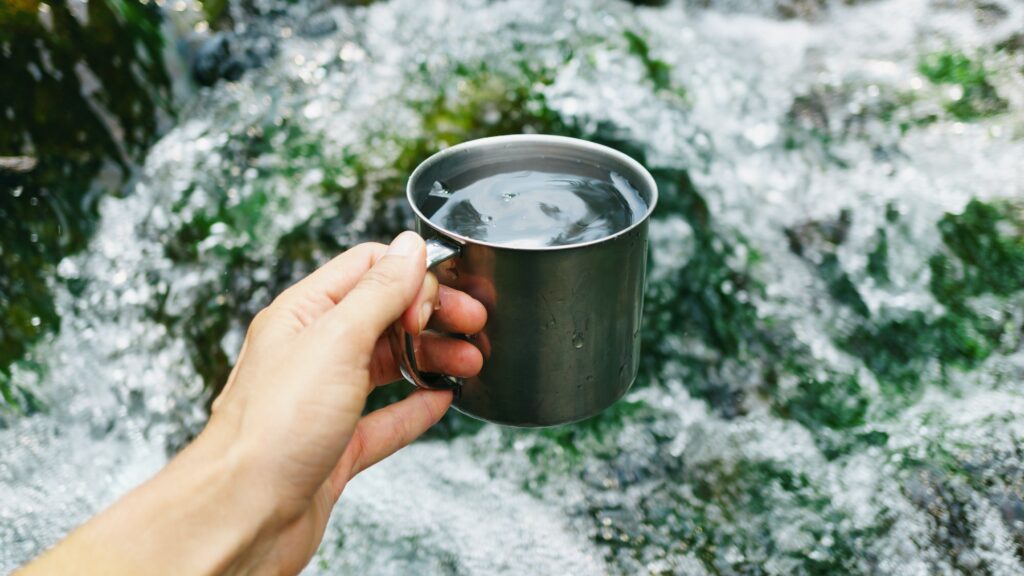 Hand holding cup with pure waterfall drinking water.