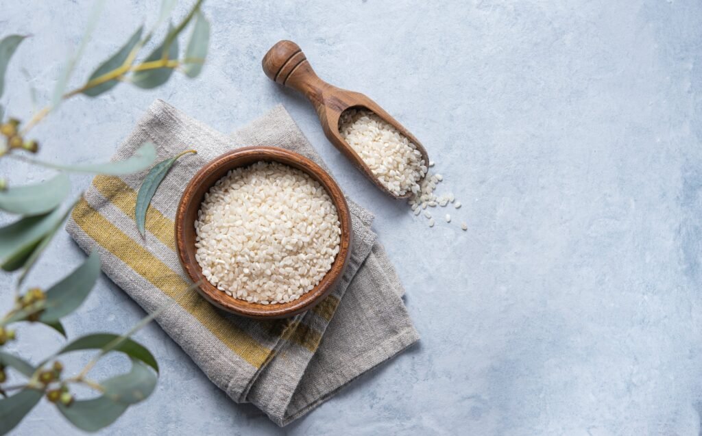 white rice Arborio in a wooden bowl on a napkin on a light blue background