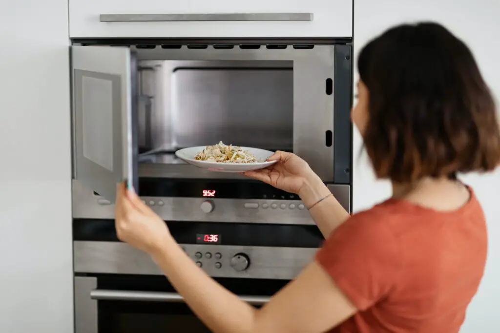 Young woman putting plate with food in the microwave oven in kitchen