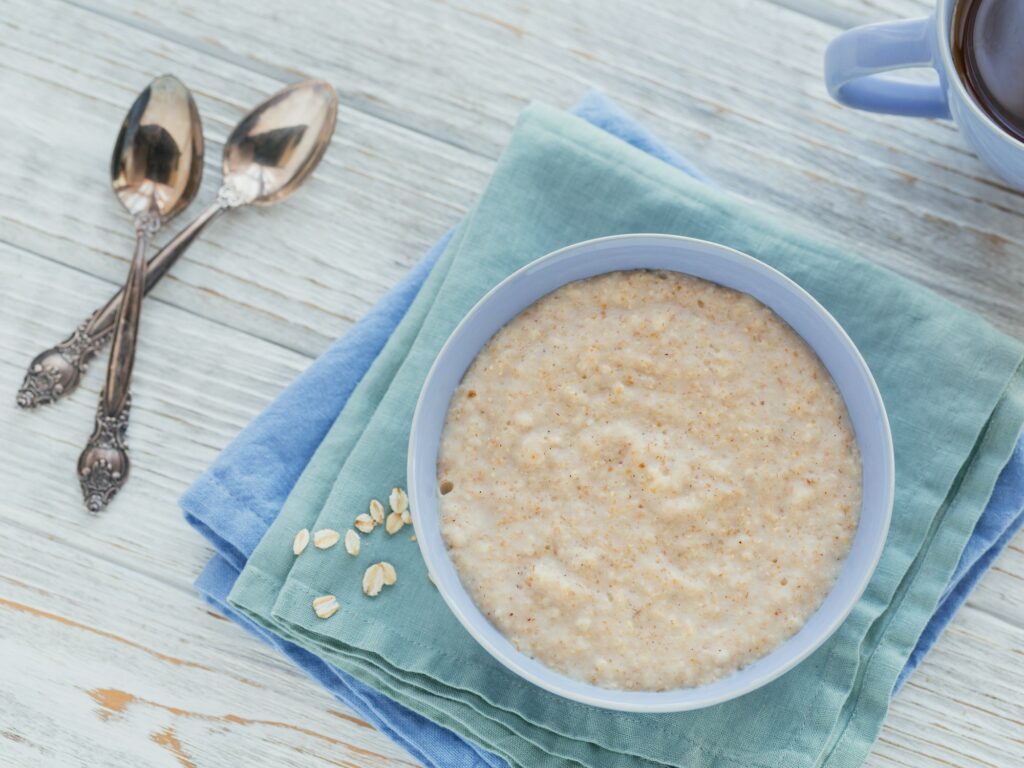Oatmeal porridge bowl on the white wooden background.