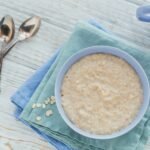 Oatmeal porridge bowl on the white wooden background.