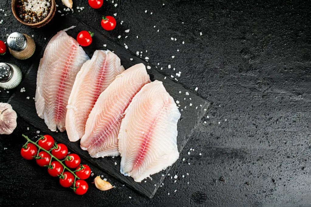 Raw fish fillet with spices and tomatoes on a stone board.