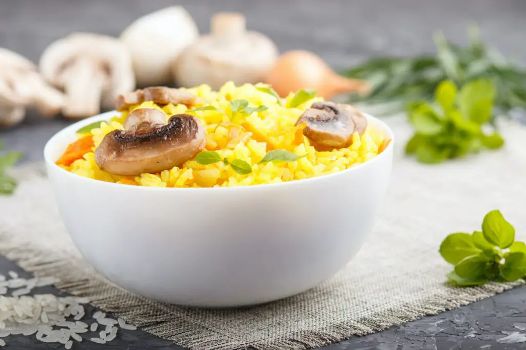 Yellow fried rice with champignons mushrooms, turmeric and oregano in white ceramic bowl